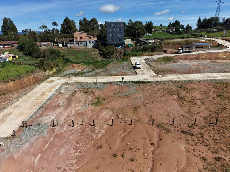 Lotes con la vía en concreto, casas vecinas y un edificio al fondo